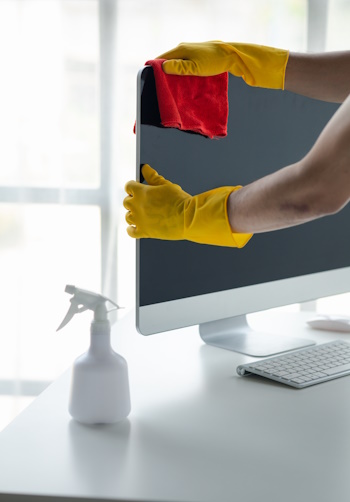 Person cleaning room, cleaning worker is using cloth to wipe computer screen in company office room. Cleaning staff. Concept of cleanliness in the organization.